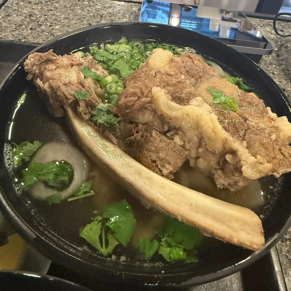 Close-up of a large bowl of Pho-Chau pho with a beef bone, meat, and fresh herbs.