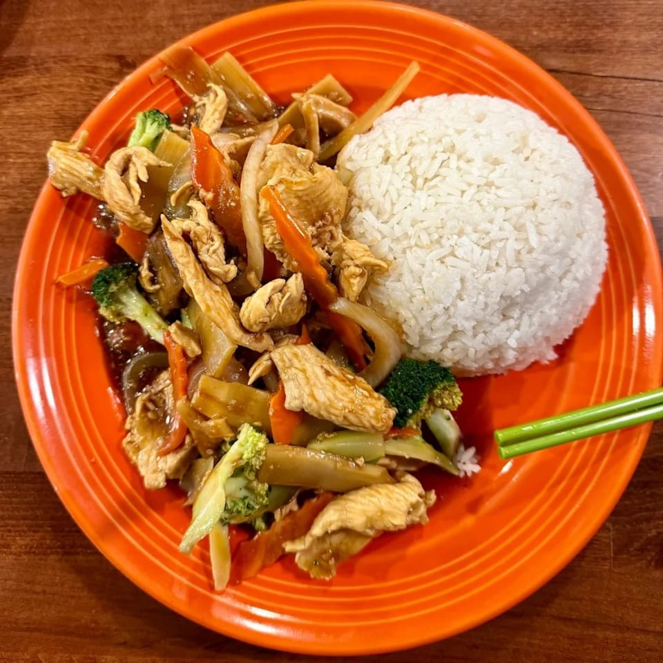 Vietnamese chicken stir-fry with broccoli, carrots, and onions, served with white rice and green chopsticks.