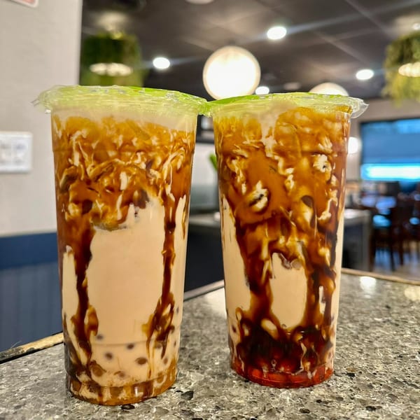 Two bubble tea drinks with brown sugar syrup streaks and light green lids on a speckled countertop.