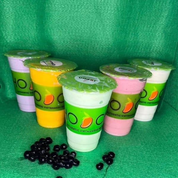 Five colorful Pho-Chau bubble tea drinks in branded cups with tapioca pearls on a green surface.