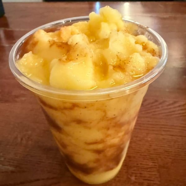 A close-up of a Vietnamese mango smoothie with brown swirls in a clear plastic cup.